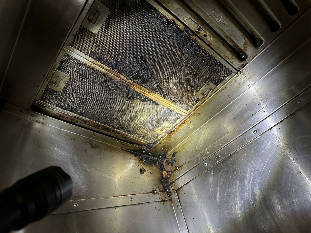 Vervuilde afzuigkap in restaurantkeuken met vetophoping en vuile filters die professionele reiniging nodig hebben