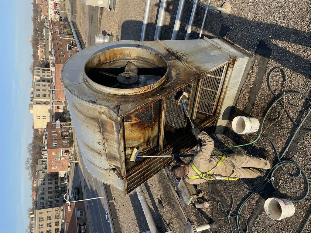 Professionele schoonmaker reinigt industriële afzuigunit op commercieel dak met gespecialiseerde apparatuur