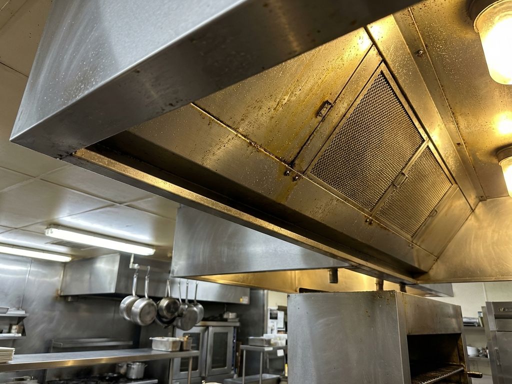 Roestvrijstalen afzuigkap in professionele restaurantkeuken met vetophoping en stofdeeltjes op filters