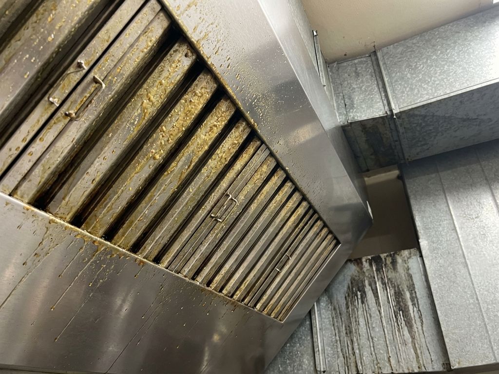 Commerciële afzuigkap van onderaf met zichtbare vetophoping en geel-bruine afzettingen op metalen roosters
