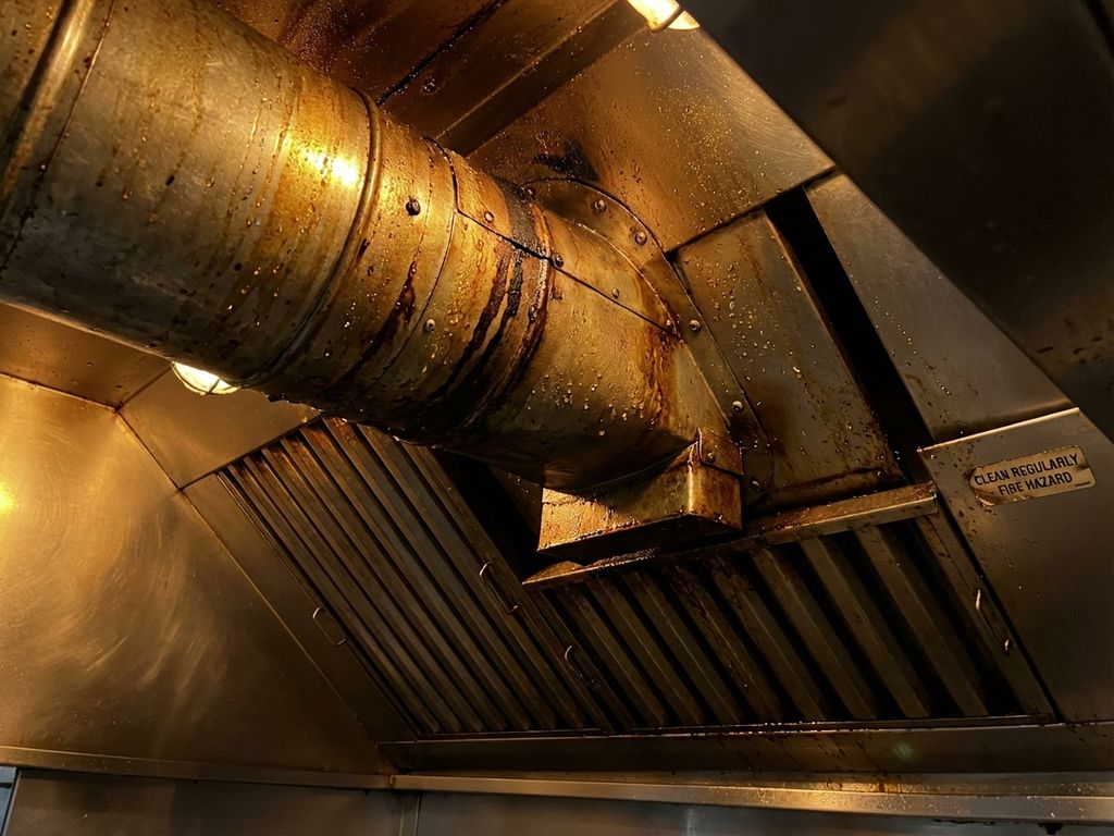 Vervuilde afzuigkap in commerciële keuken met vetafzetting en olieresten op roestvrijstalen oppervlakken