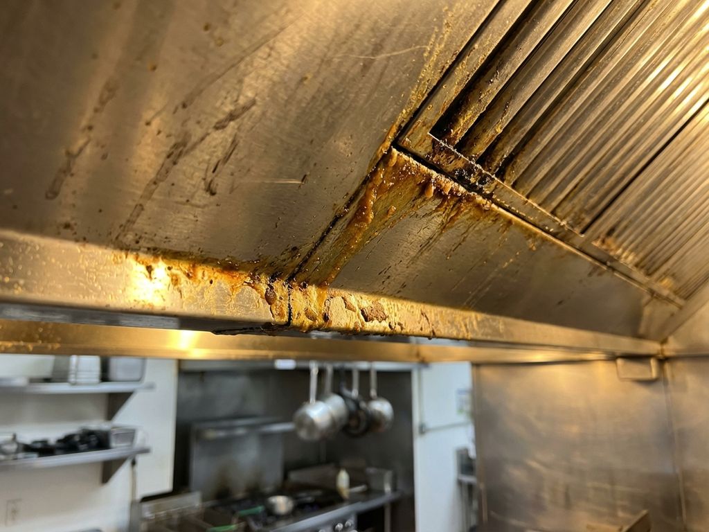 Commerciële restaurantafzuigkap met vetaanslag en vuil rond filters, onderhoudswerk vereist in professionele keuken