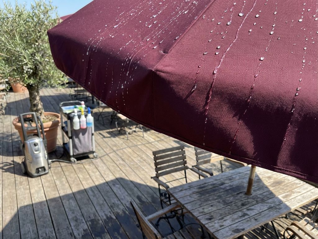 Bordeauxrode parasol met waterafstotende behandeling op zonnig restaurantterras met houten meubilair