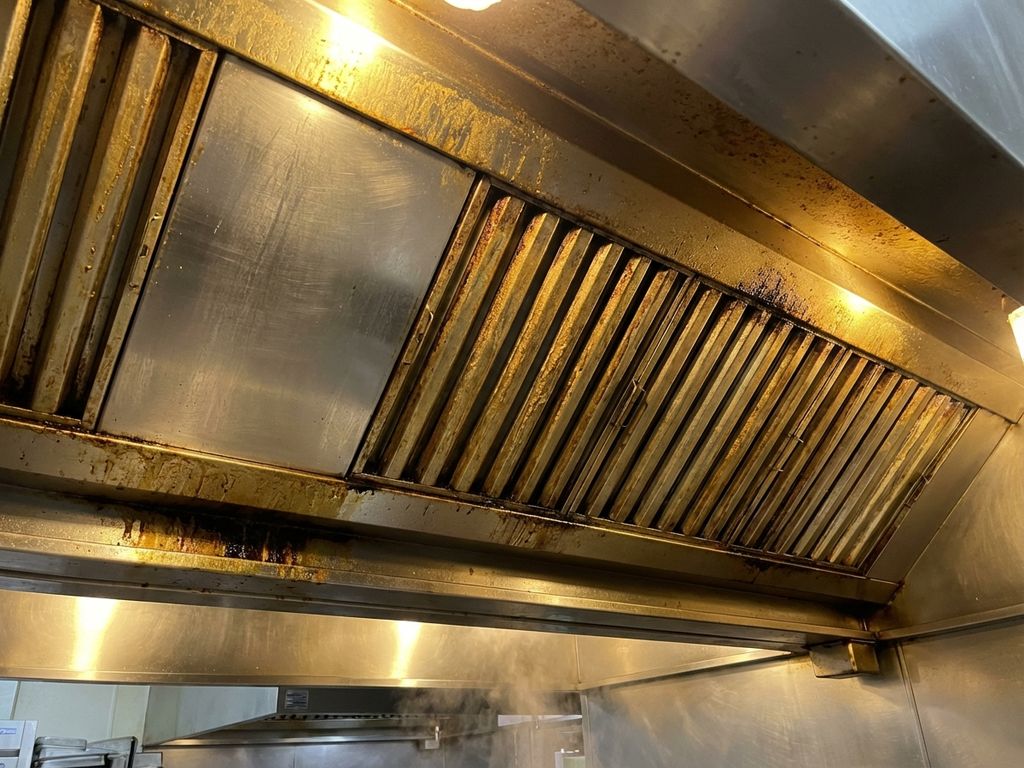 Roestvrijstalen afzuigkap in restaurant met vetophoping en verkleuring op filters, contrast tussen schone en vervuilde delen