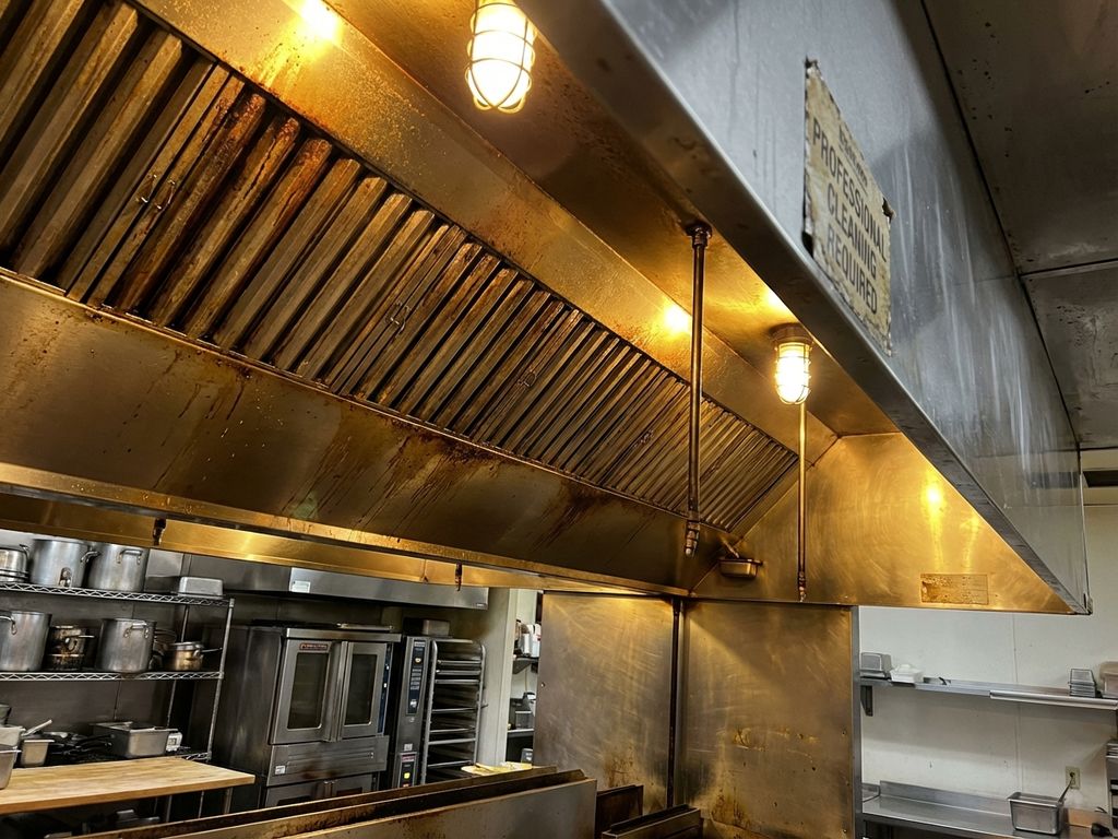 Professionele roestvrijstalen afzuigkap in restaurantkeuken met vetophoping en slijtage, onderaanzicht