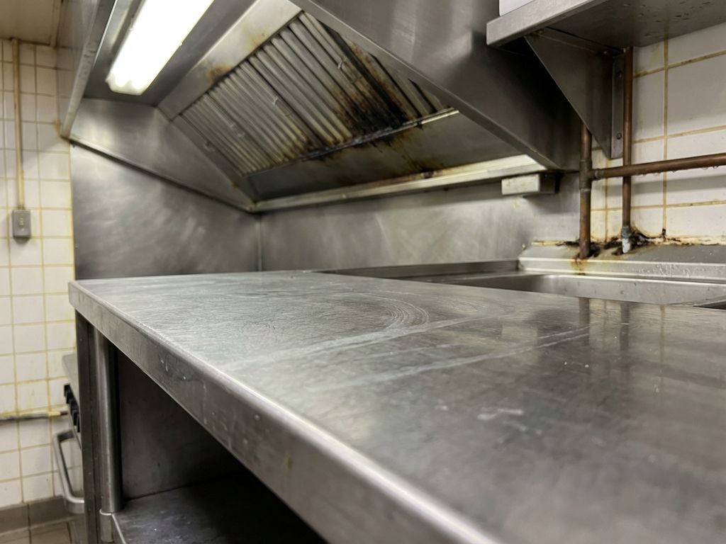 Professionele restaurantkeuken met roestvrij staal, watervlekken en vochtige plekken rond gootsteen en leidingen