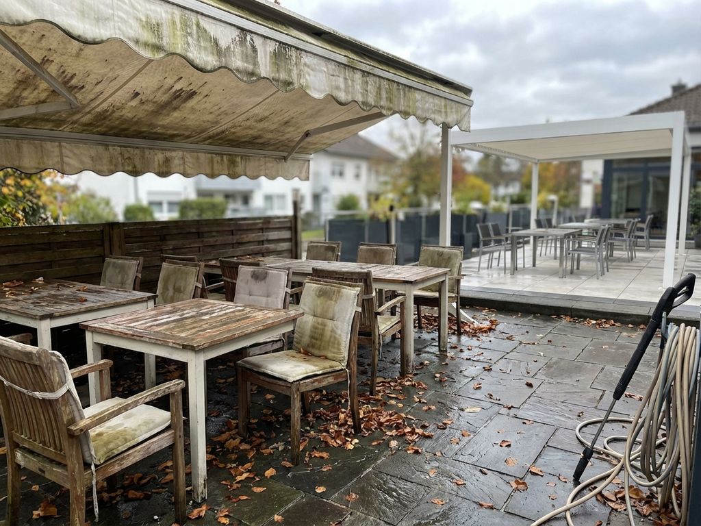 Vervuild restaurantterras met verweerde houten meubels contrasteert met schoon modern terras op de achtergrond