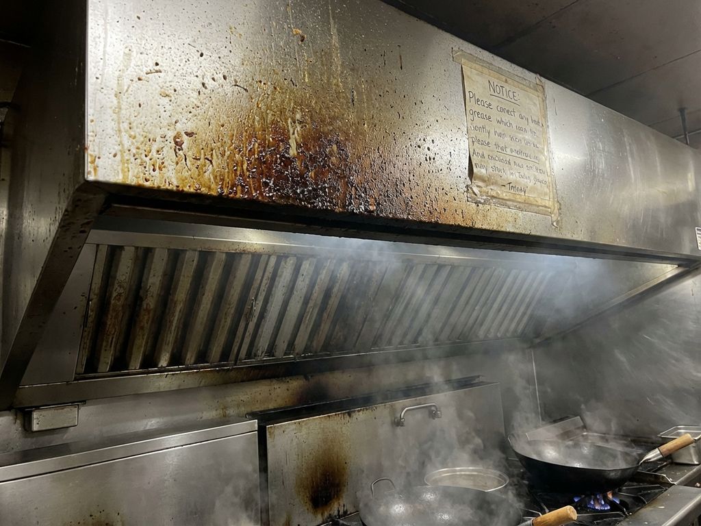 Commerciële wokstation met vetaanslag en rookresten op roestvrijstalen afzuigkap in professionele keuken