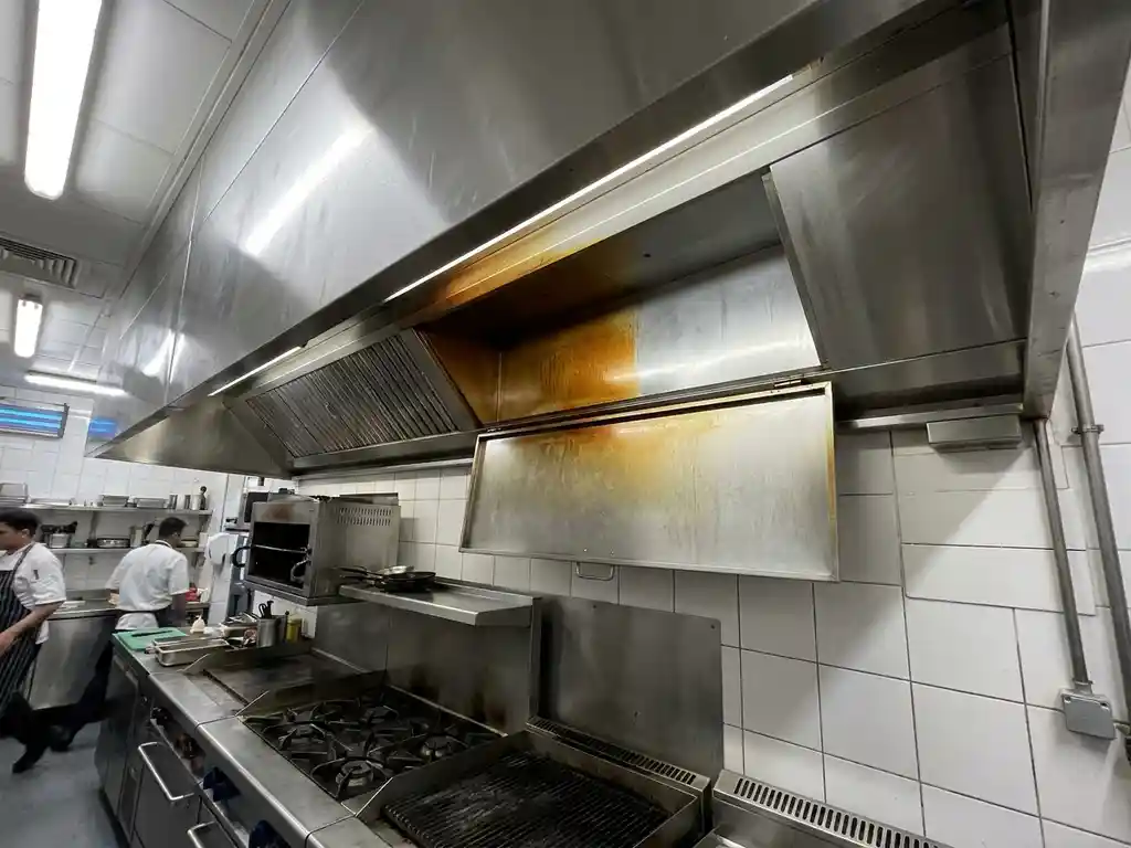 Roestvrijstalen afzuigkap boven professioneel fornuis met zichtbaar vetaanslag aan één zijde en glanzend schoon metaal aan de andere.